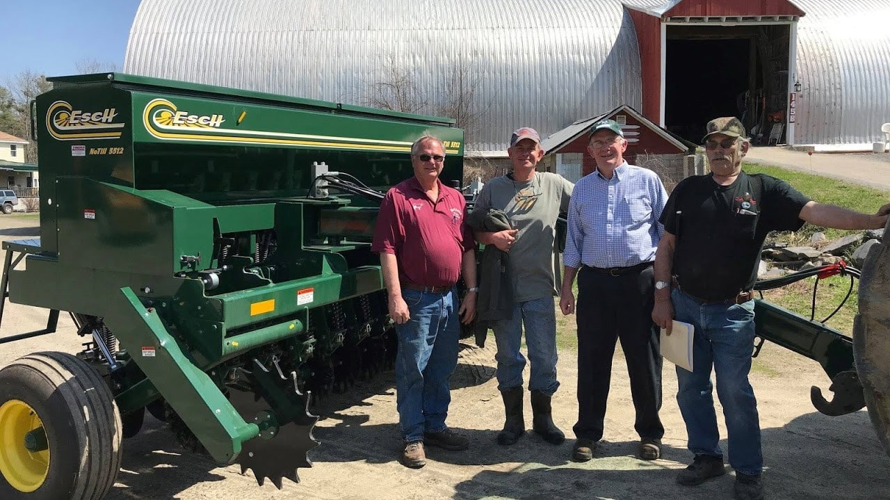 Four men stand next to a no-till seeder.